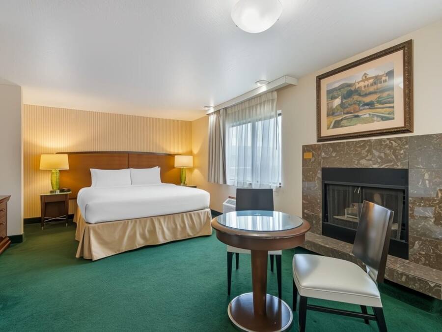 Een hotelkamer met een bed, een ronde tafel met een stoel, een open haard en een schilderij aan de muur.