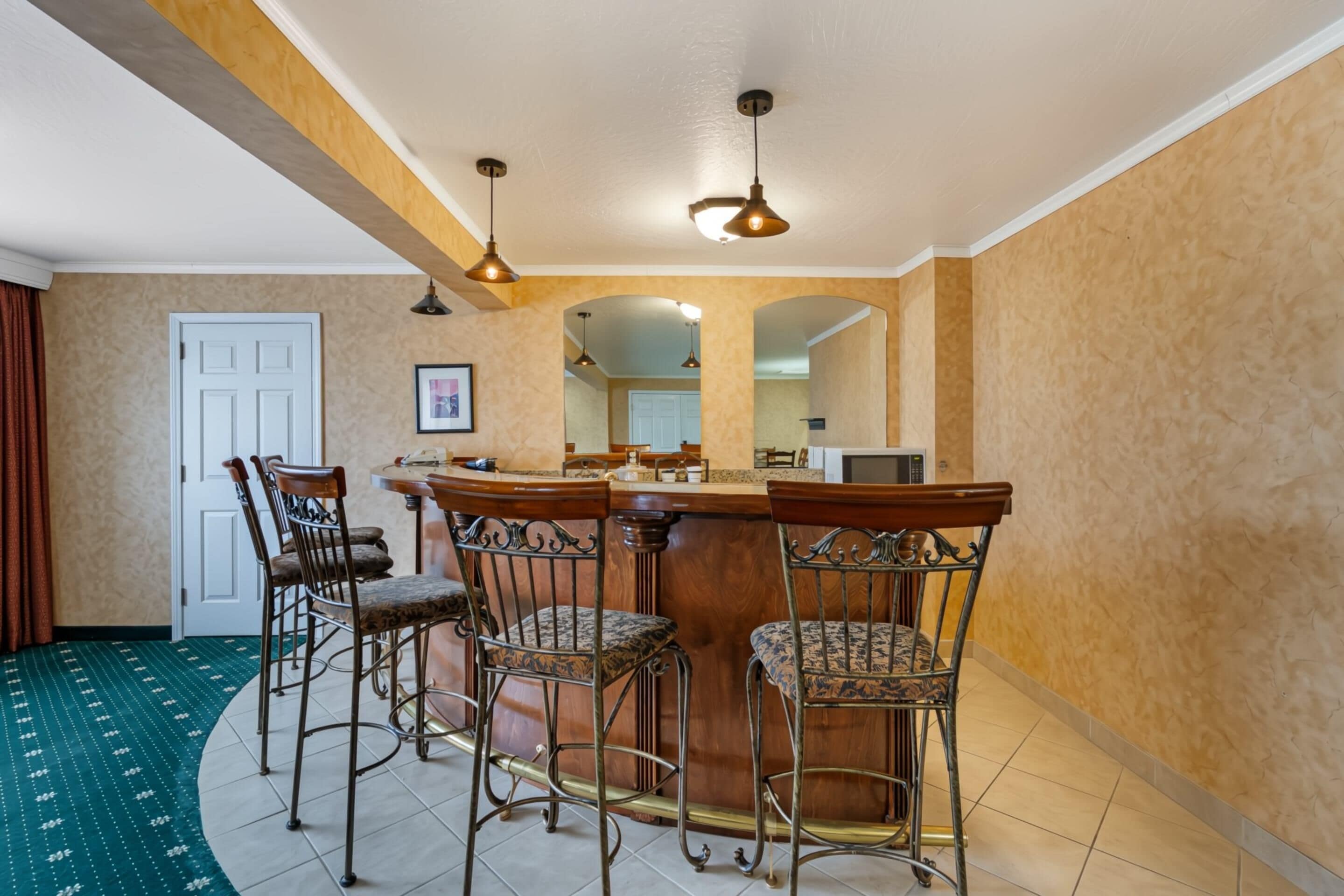 A dining area with a bar, four chairs, and pendant lighting.