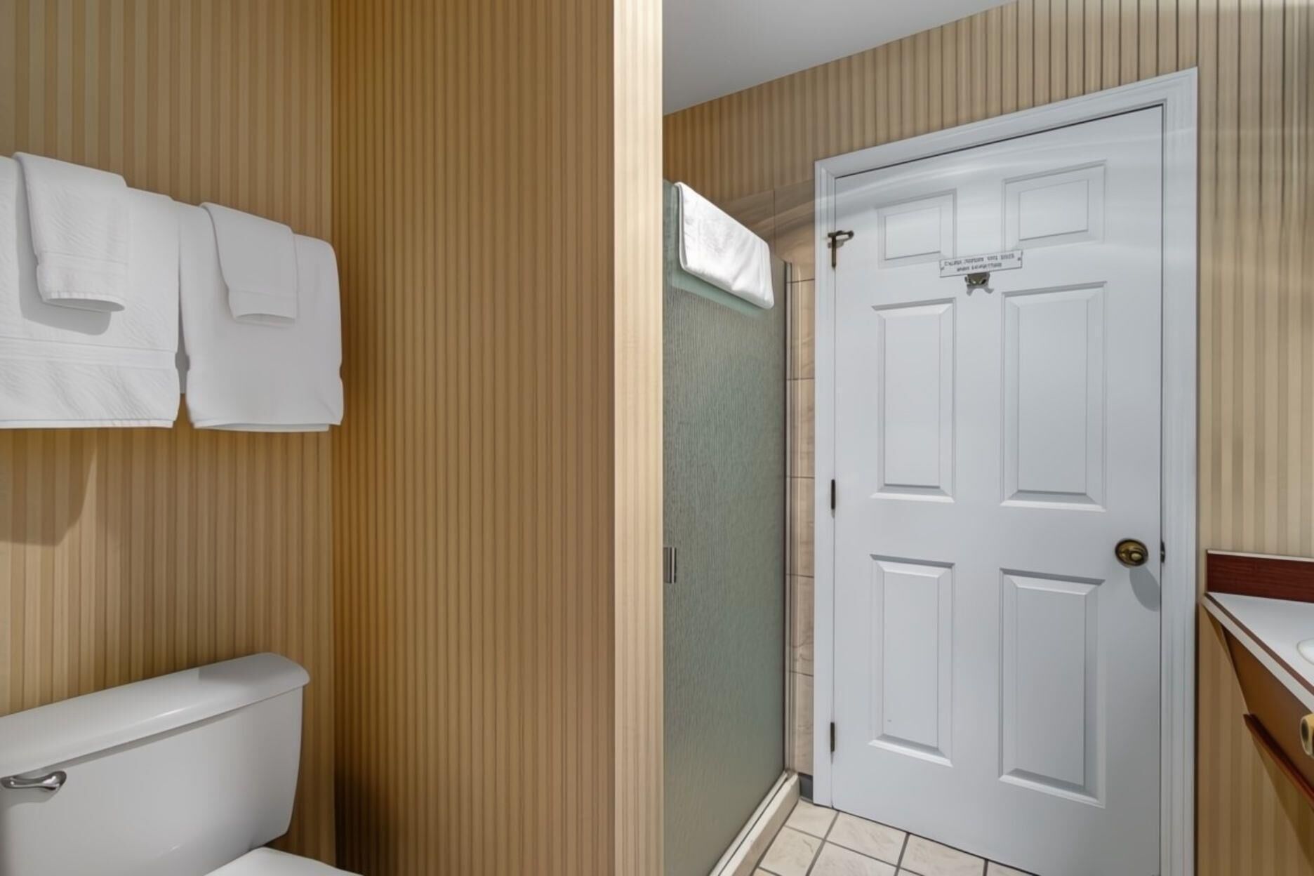 A bathroom with a toilet, a towel rack with towels, and a door.