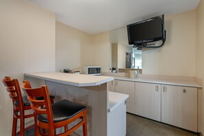 Een kleine keuken met een magnetron, een kleine koelkast en een flatscreen televisie aan de muur.