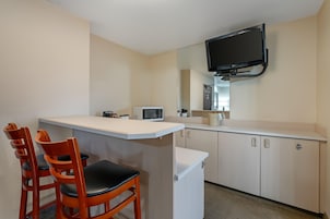 Una kitchenette compacta con microondas, un refrigerador pequeño y un televisor de pantalla plana montado en la pared.