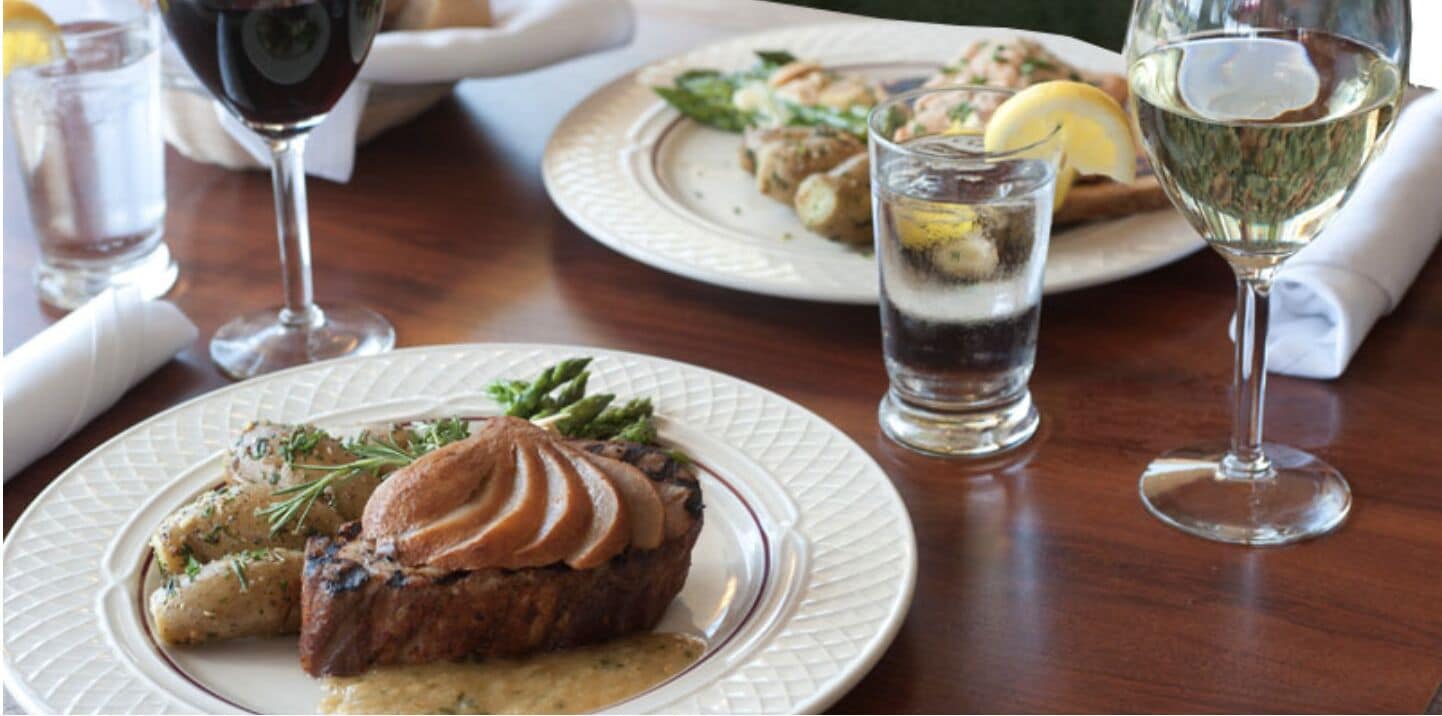 A dining table with plates of food, glasses of water and wine, and a napkin.