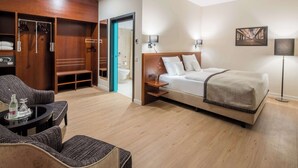 A hotel room with a bed, a seating area with chairs, a wooden wardrobe, and a bathroom visible through an open door. - Best Western Plus Hotel Excelsior (Erfurt)