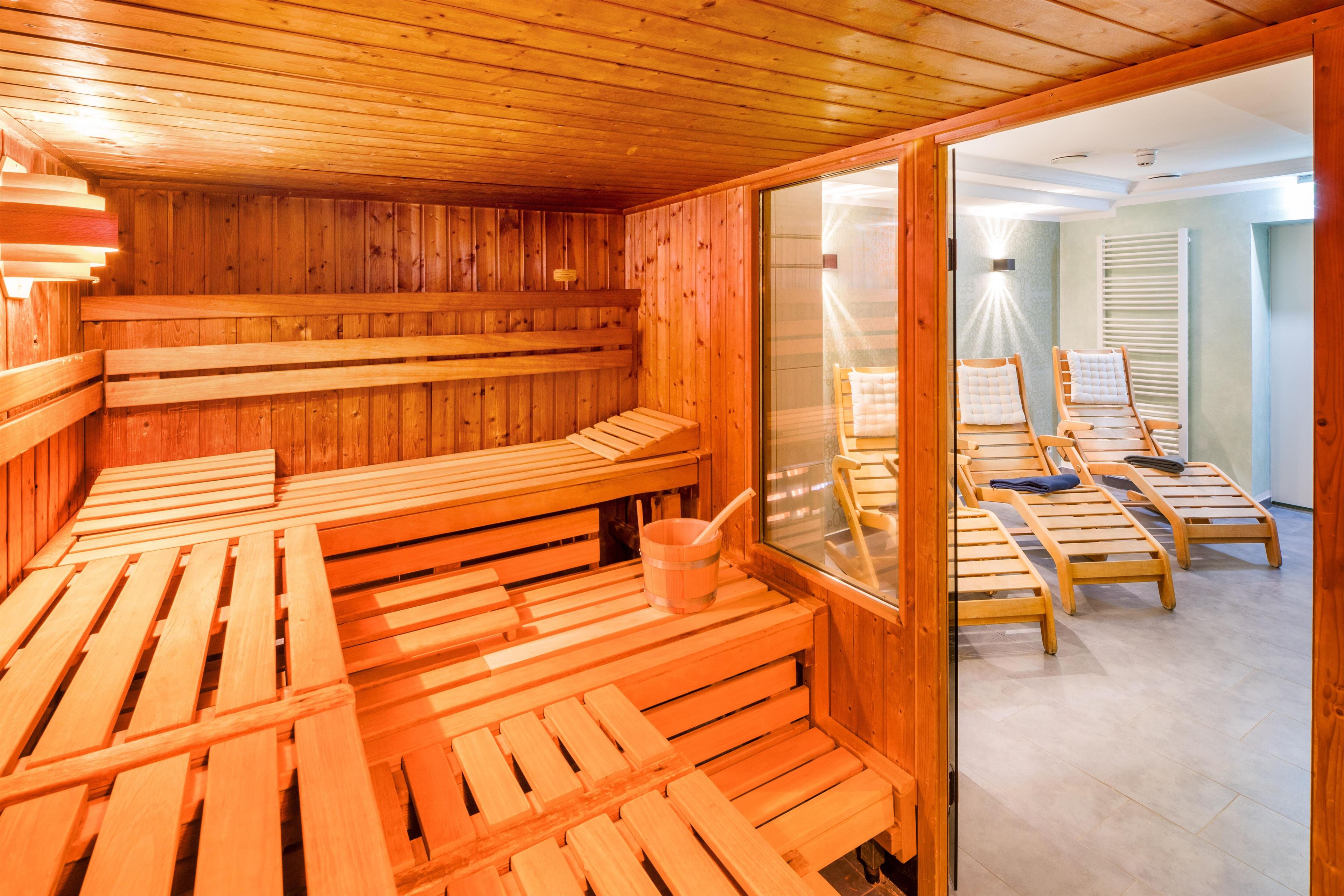 A sauna with wooden benches and a glass door leading to a room with chairs and a window.