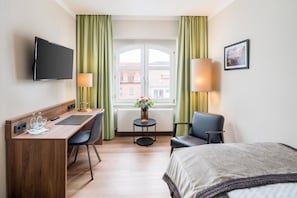 A hotel room with a bed, desk, two chairs, a TV, a small table with a vase of flowers, and a window with curtains. - Best Western Plus Hotel Excelsior (Erfurt)