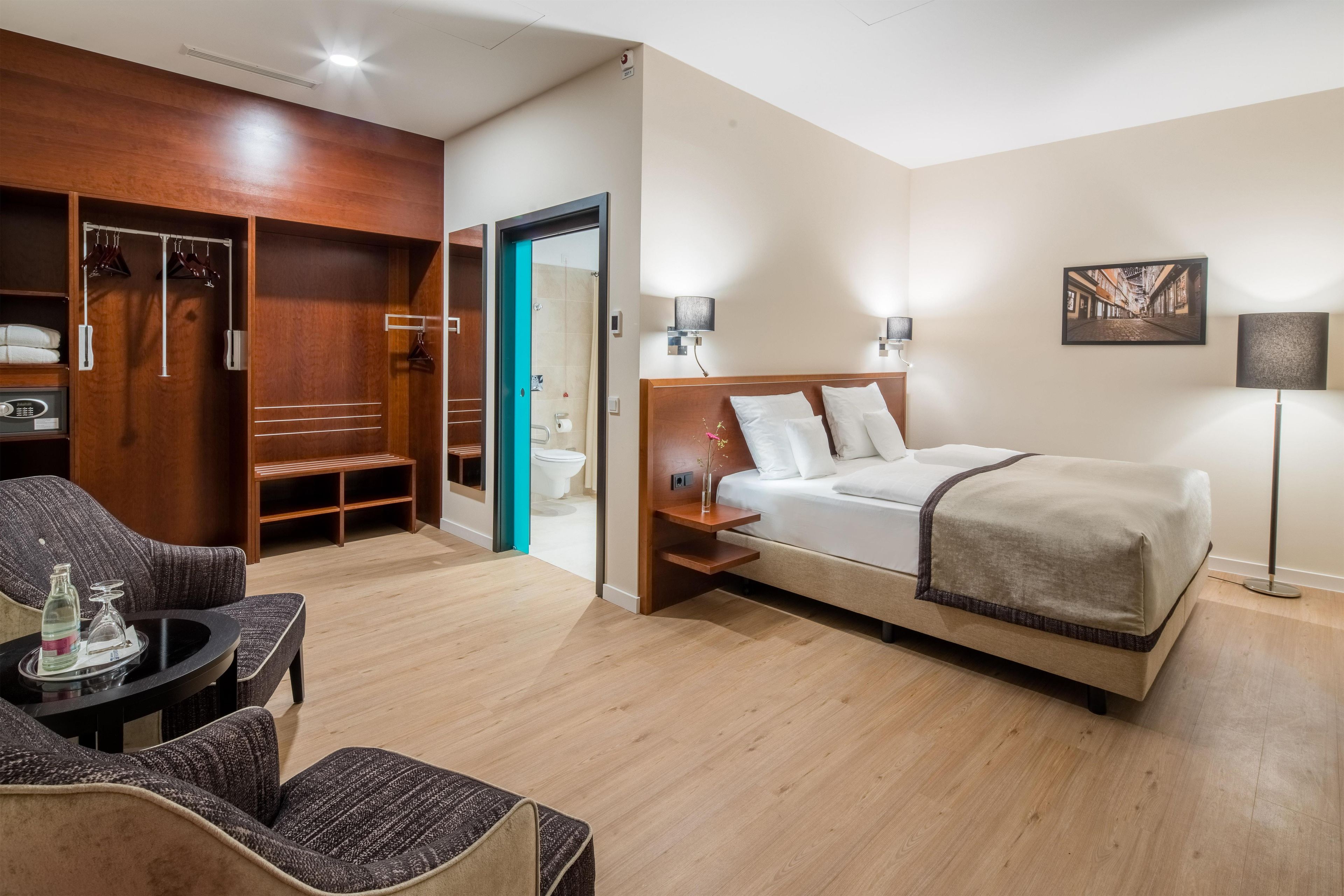 Habitación de hotel con cama, zona de estar con una silla, armario y baño.