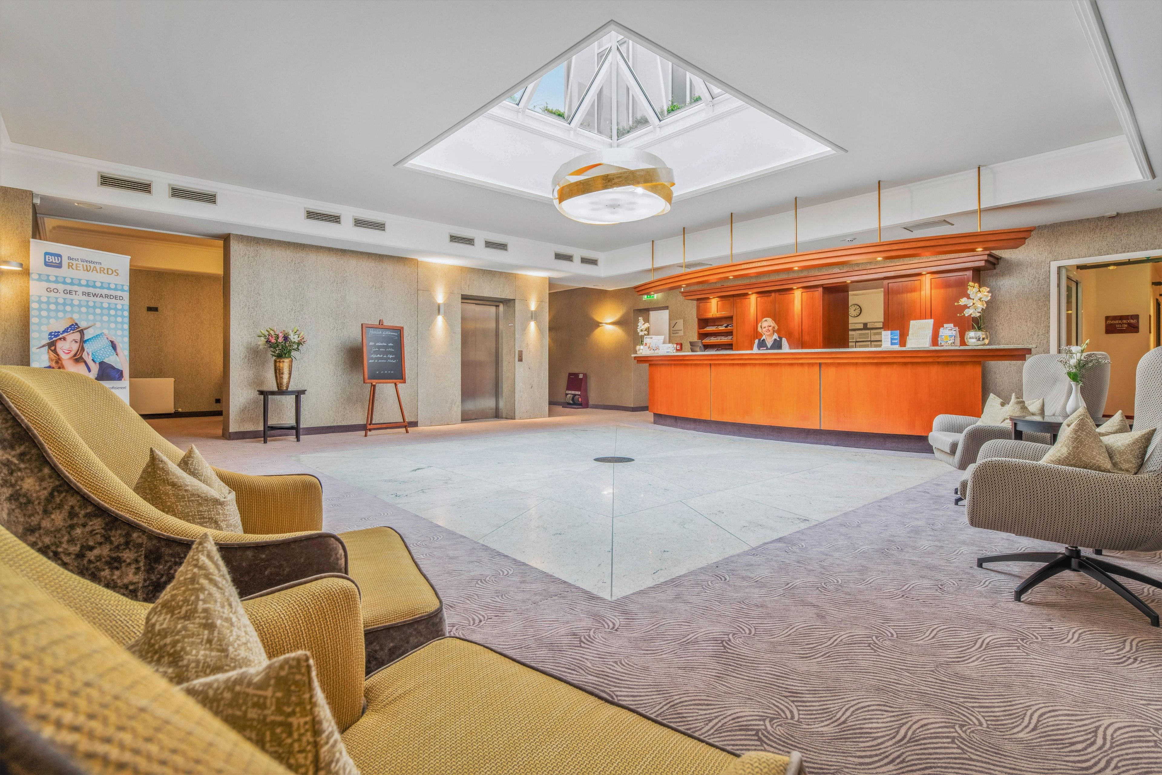 A hotel lobby with a reception desk, seating area, and a large skylight.
