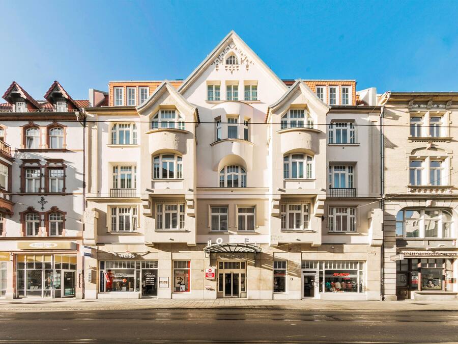 Et hotel i flere etager med klassisk arkitektur, der har en central indgang og mange vinduer på hver etage.