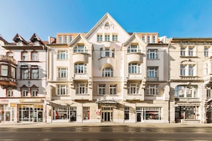 Un hotel de varios pisos con un diseño arquitectónico clásico, que presenta una entrada central y múltiples ventanas en cada planta.
