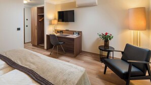 A hotel room with a bed, a desk, a chair, a TV, and an air conditioning unit. - Best Western Plus Hotel Excelsior (Erfurt)