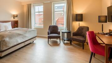 Quarto de hotel com uma cama, duas poltronas, uma escrivaninha com telefone e televisão.