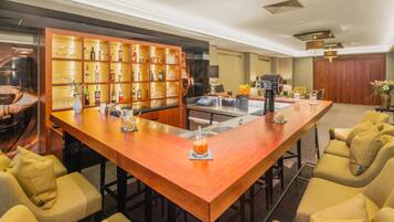 Una zona de bar con una barra de madera larga, diversas opciones de asientos y una estantería bien surtida de licores.