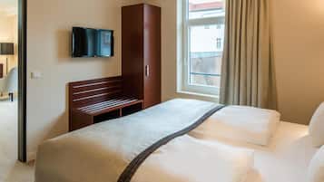 Habitación de hotel con cama, televisor montado en la pared, banca de madera y ventana con cortinas.