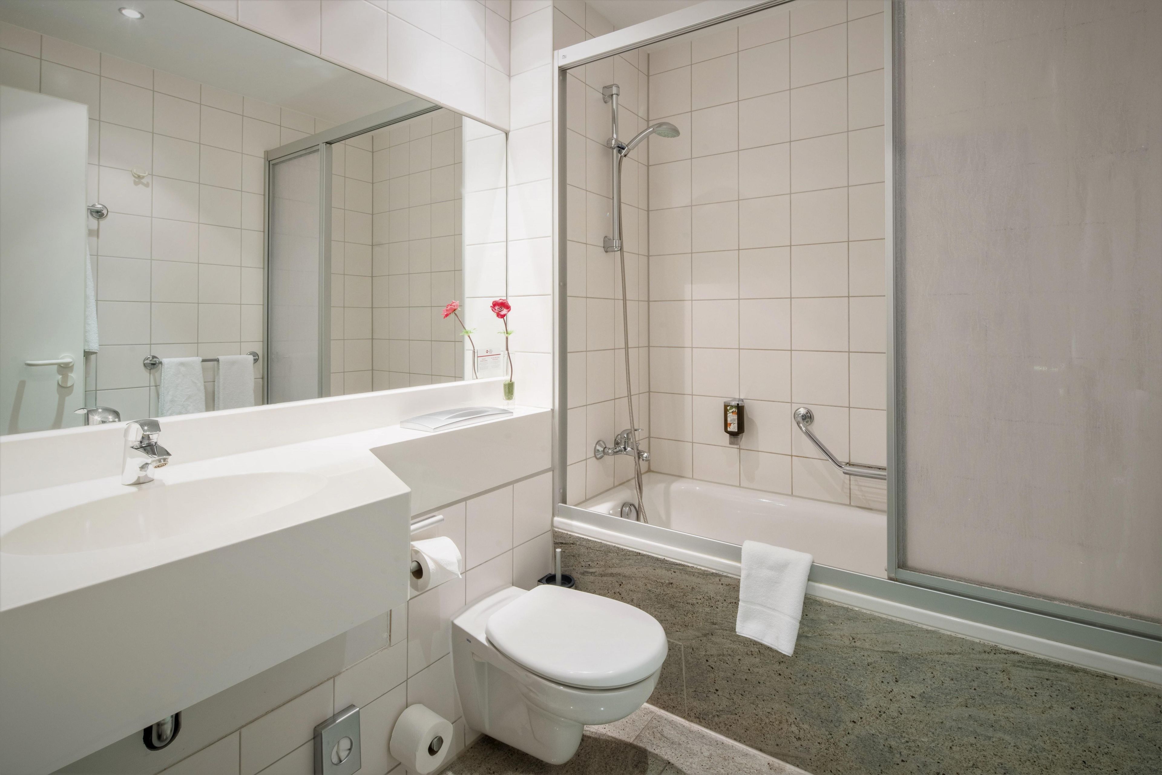 Un baño moderno con un espejo grande, un lavamanos blanco, un inodoro y una zona de ducha.