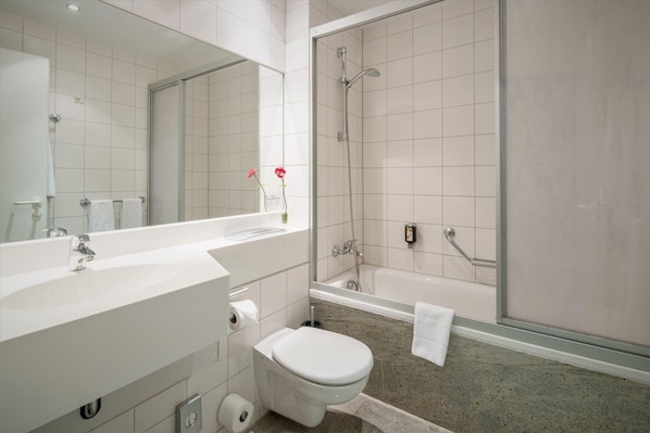 A modern bathroom with a large mirror, a white sink, a toilet, and a shower area.