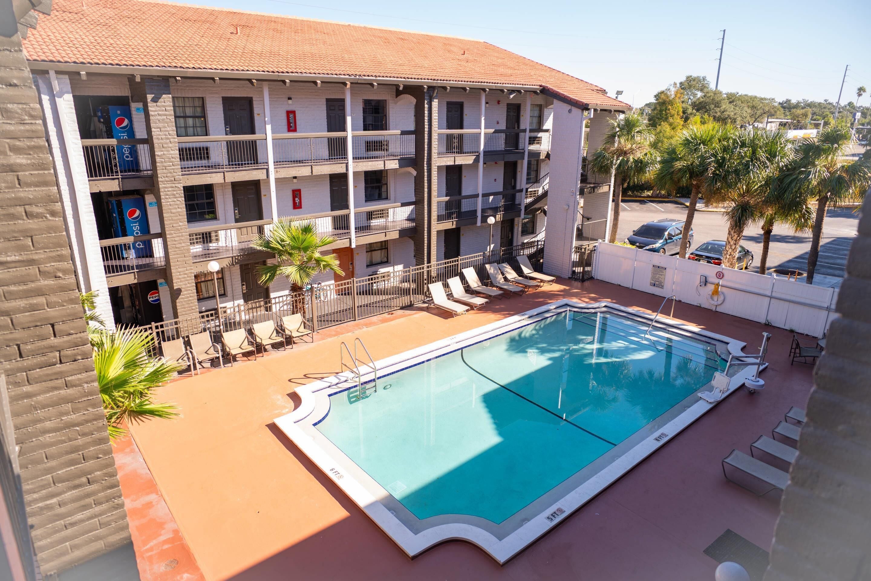 A swimming pool with lounge chairs and a building with multiple balconies.