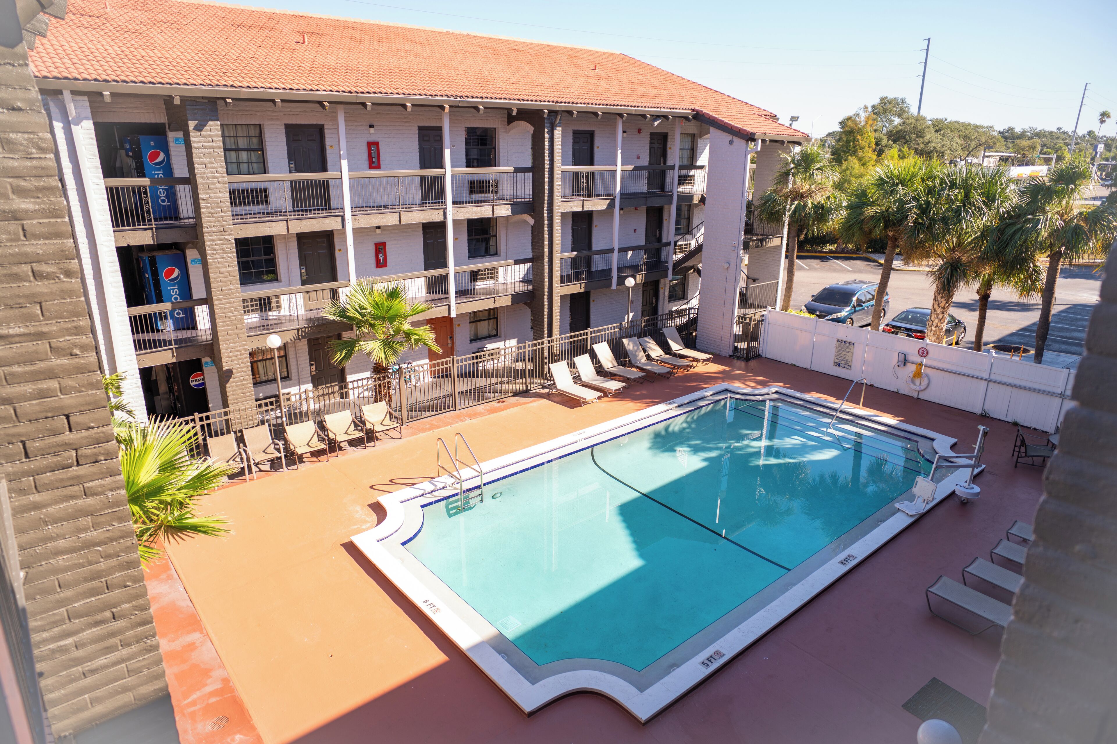 A swimming pool with lounge chairs, a building with multiple balconies, and palm trees.
