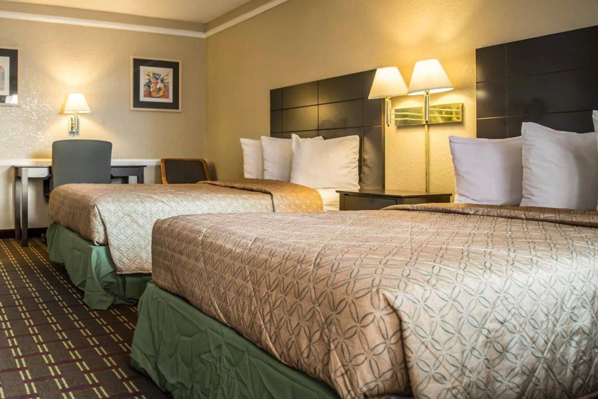 A hotel room with two beds, a desk, and two lamps.