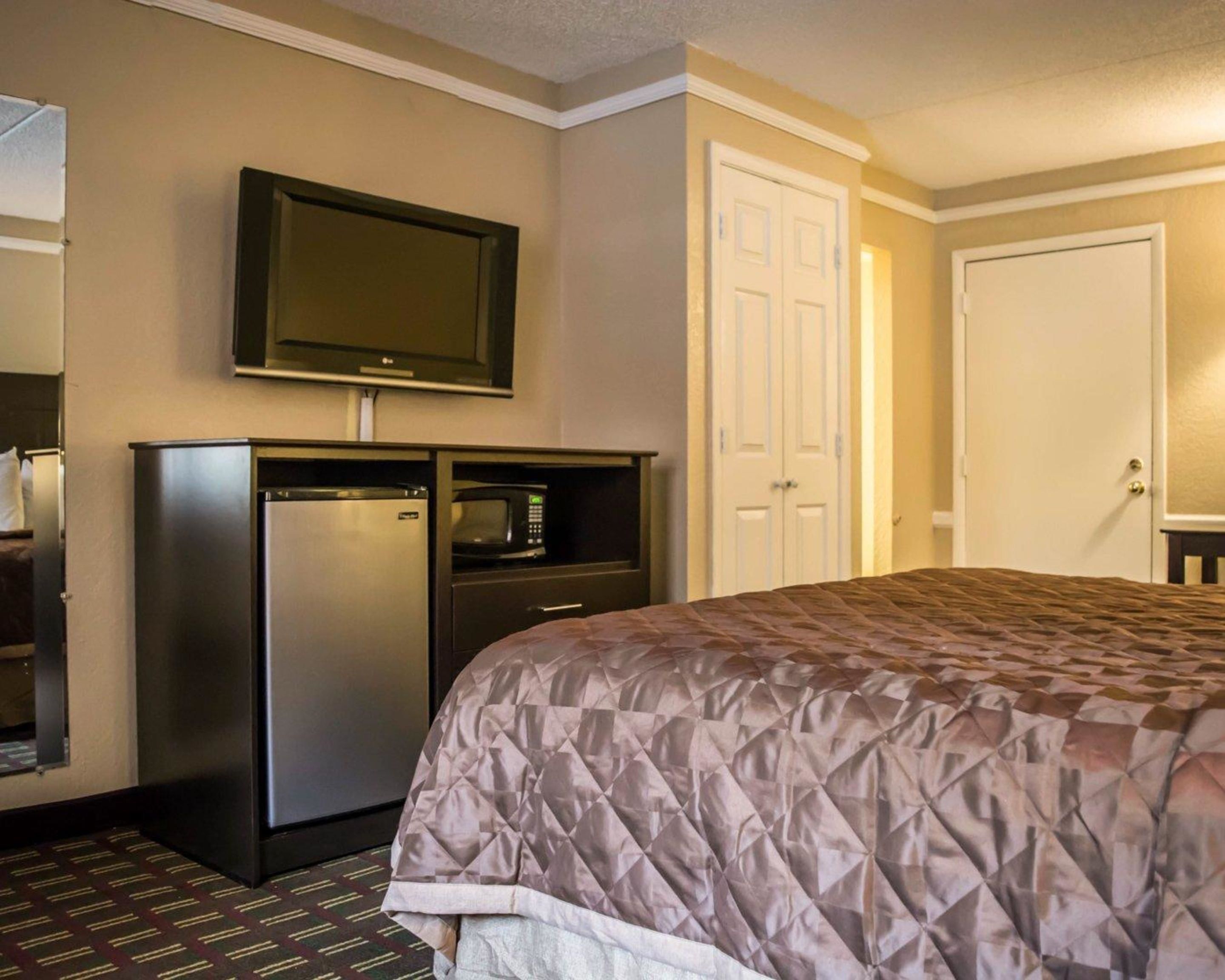 A hotel room with a bed, a television mounted above a minibar, a refrigerator, and a door to another room.