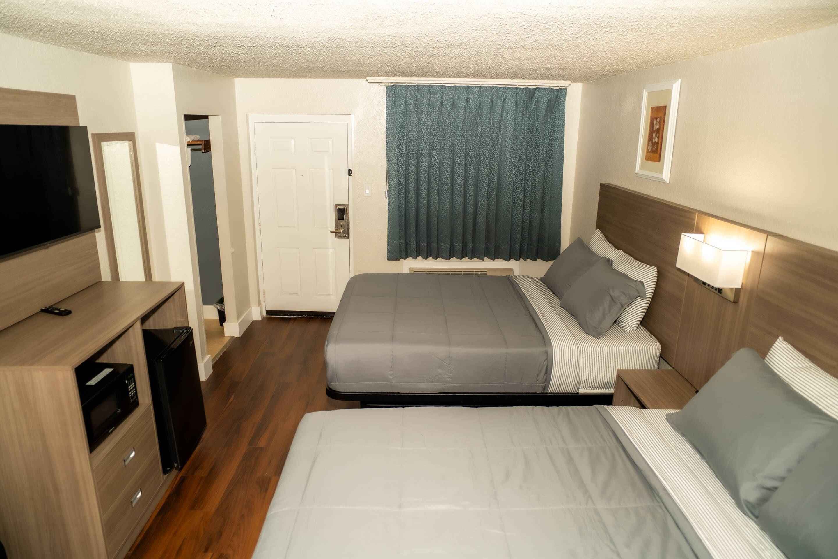 A hotel room with two beds, a TV, a microwave, and a door leading to a bathroom.