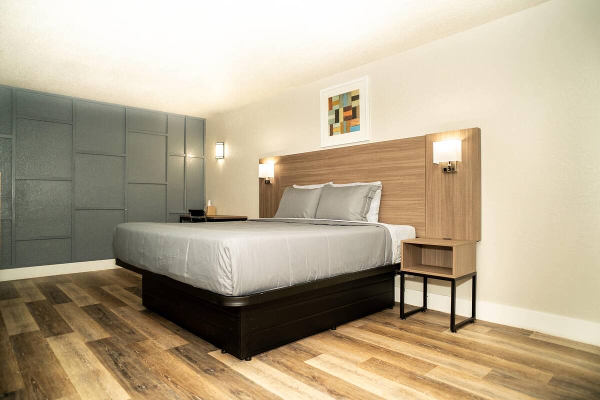 A modern bedroom with a large bed, a nightstand, a wooden headboard, and a wall-mounted light fixture.