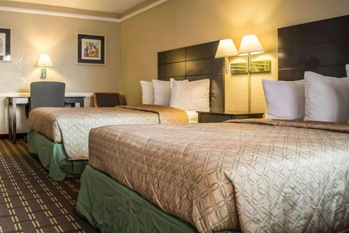 A hotel room with two beds, a desk, and two lamps.