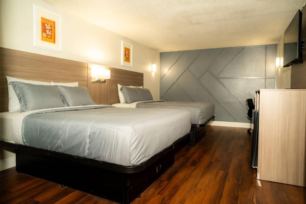A hotel room with two beds, wooden flooring, a flat-screen TV, and a small kitchenette.