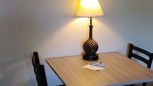 Un área de comedor con una mesa, sillas, una lámpara y una obra de arte enmarcada en la pared.