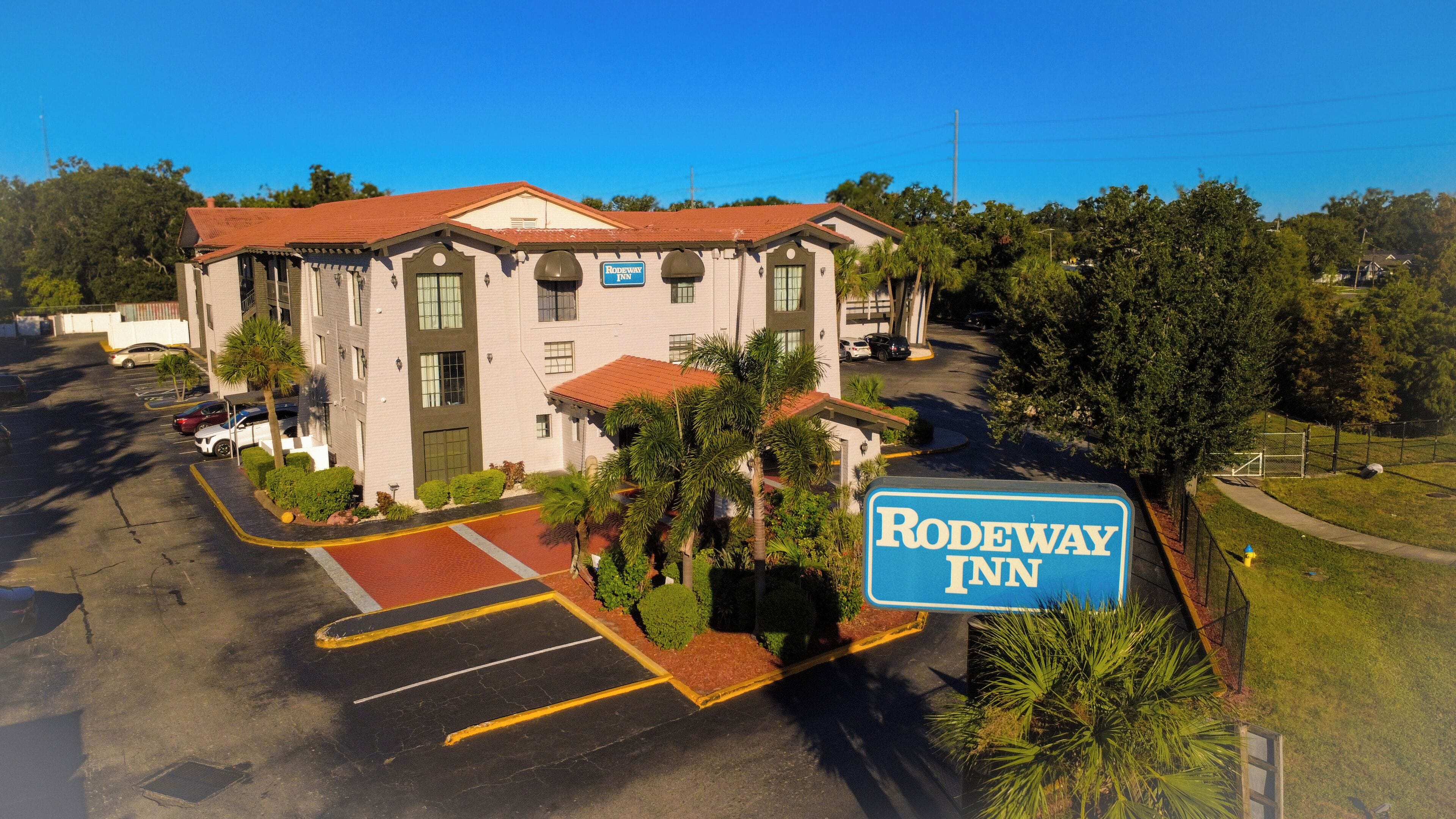 Ein Rodeway Inn mit Parkplatz, Palmen und blauem Himmel.
