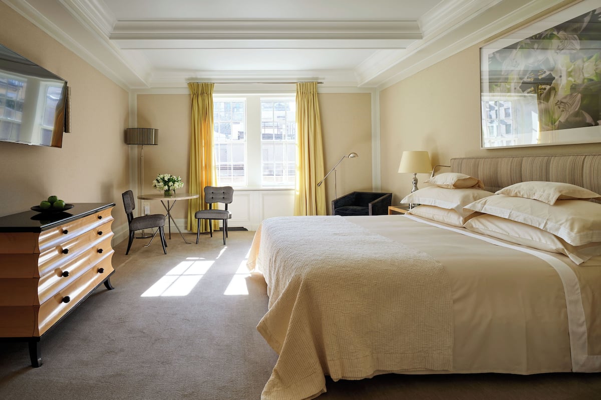 A hotel room with a large bed, a dresser, a chair, a desk, and a window with curtains.