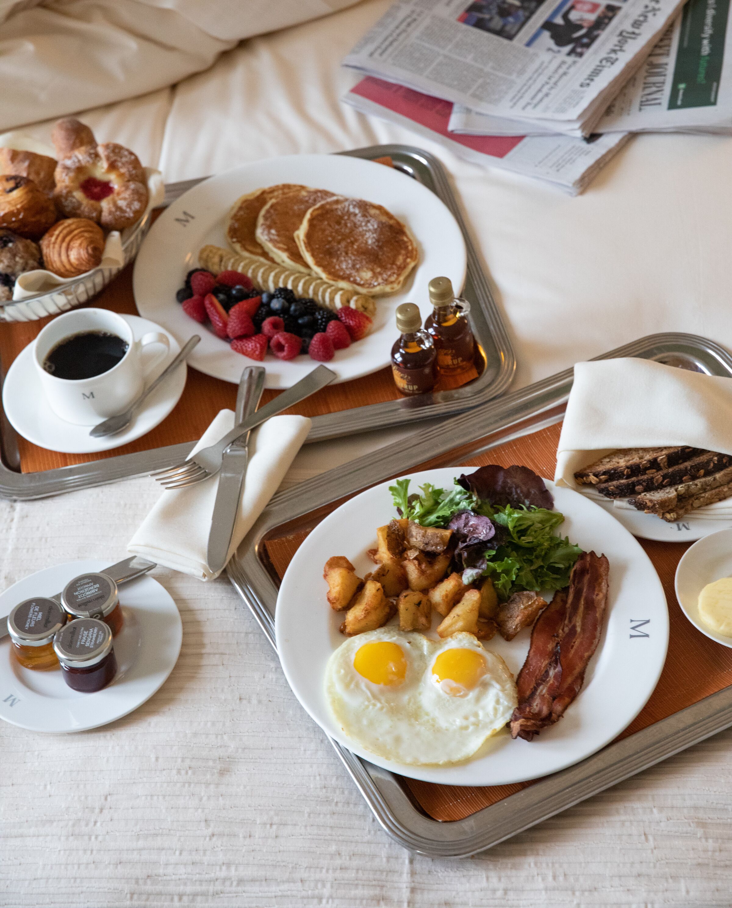 A breakfast tray with pancakes, eggs, bacon, toast, and fruit on a bed.