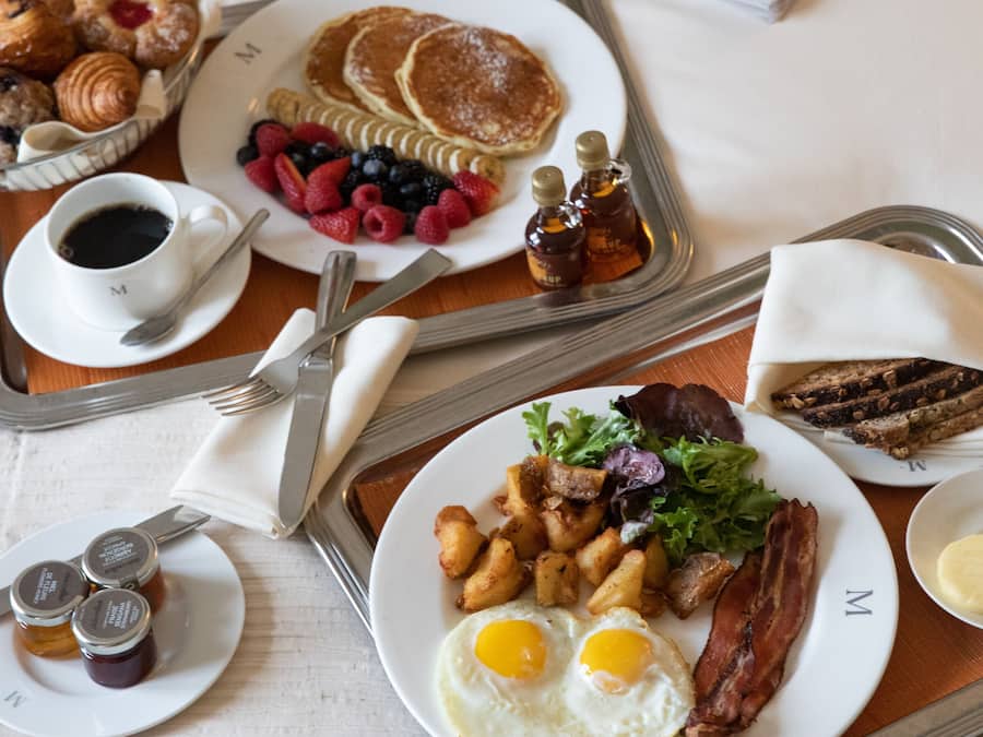A breakfast tray with pancakes, eggs, bacon, toast, and fruit on a bed.