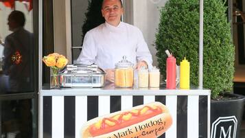 A street food cart named "The Mark Hotdog" with a chef behind it, featuring a large hotdog graphic and condiment bottles.