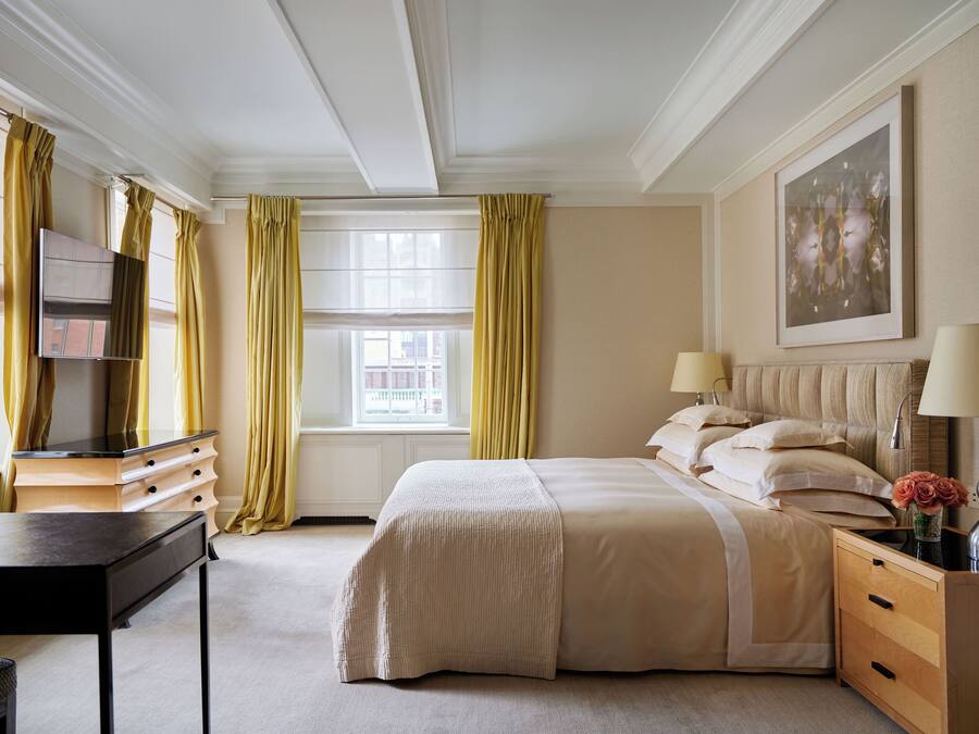 Een keurig opgemaakt slaapkamer met een bed, nachtkastjes, een bureau en een raam met gordijnen.