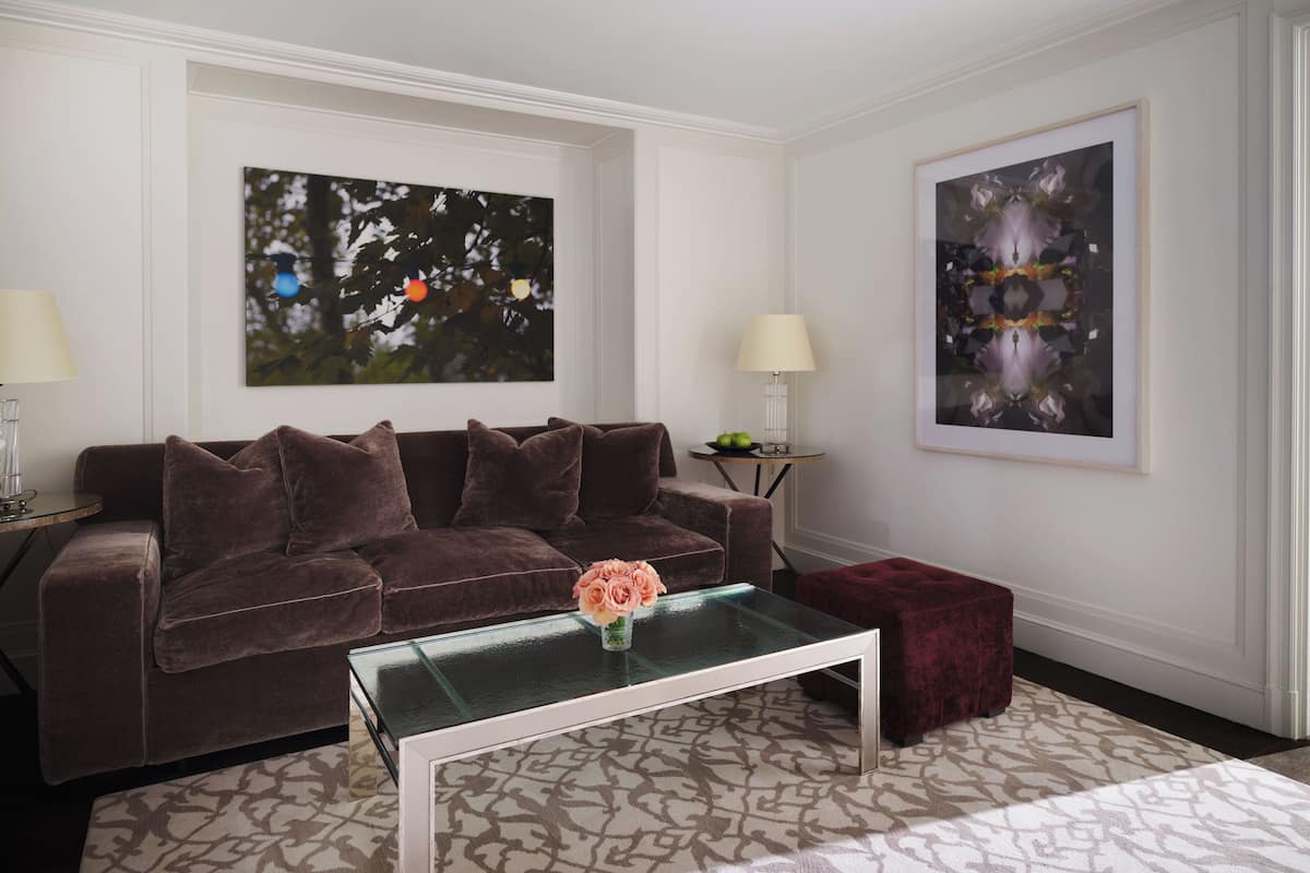 A living room with a brown sofa, a glass coffee table with a vase of flowers, and two framed abstract paintings on the walls.