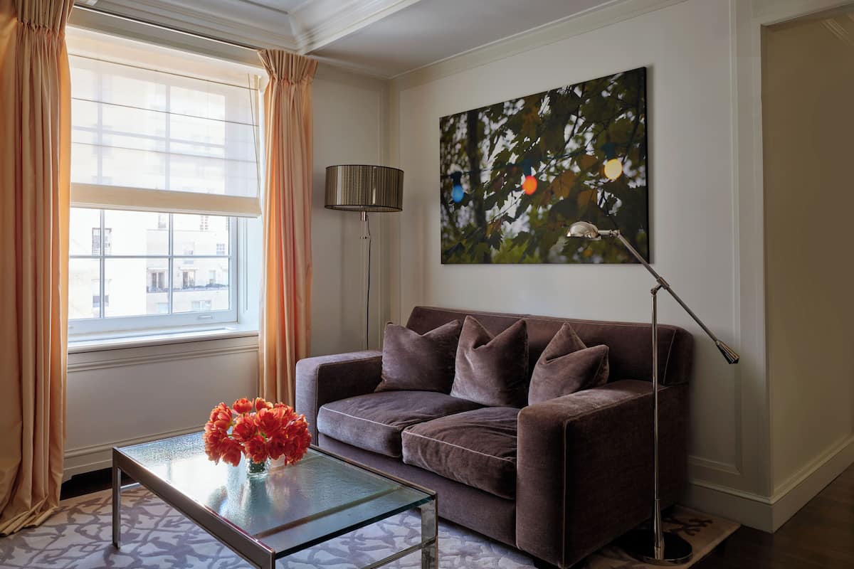 A living room with a sofa, a glass coffee table with flowers, a floor lamp, and a painting on the wall.