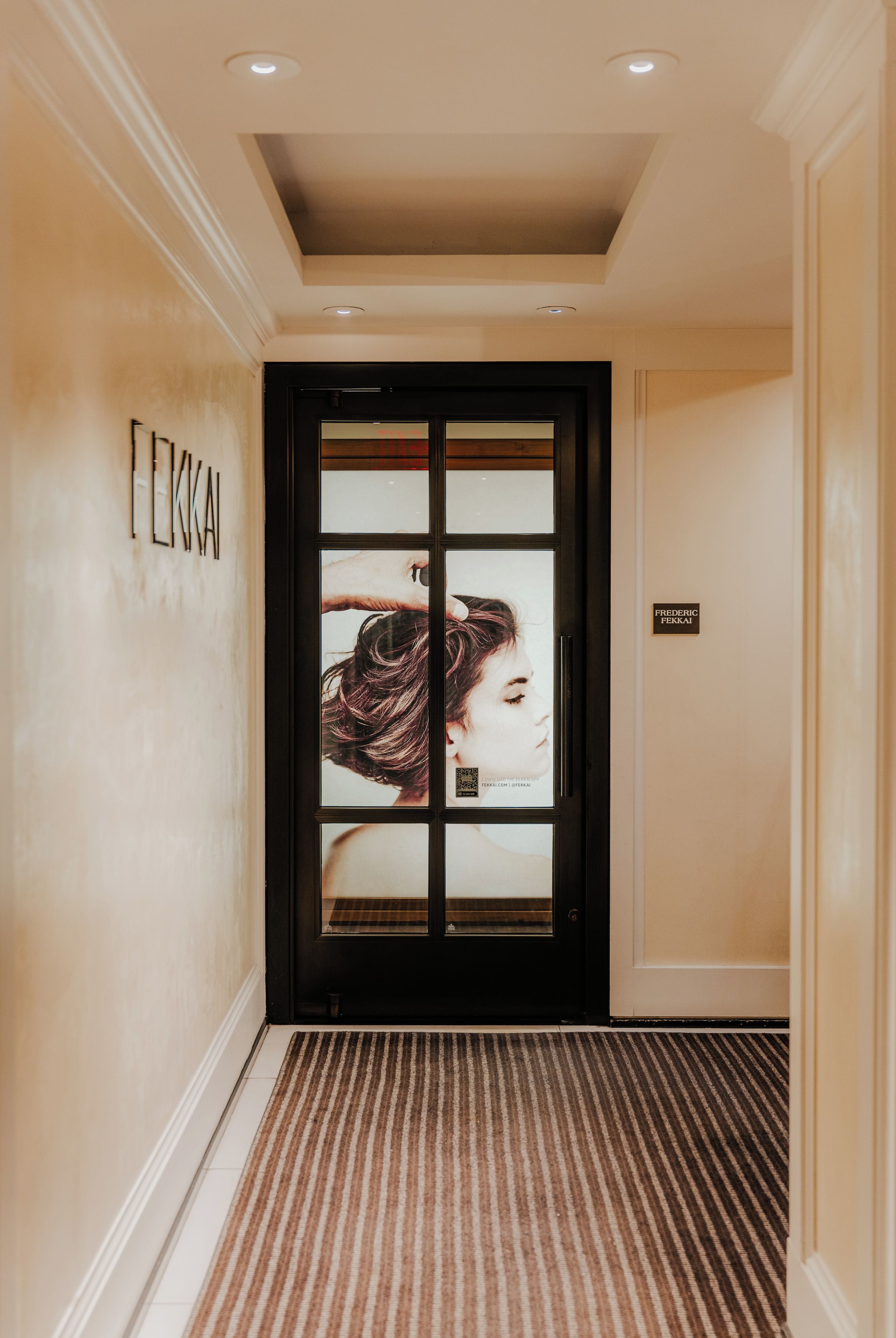L’entrée d’un hôtel, avec une porte sombre, une enseigne indiquant « FREDERIC FEEKKA » et un tapis à motifs.