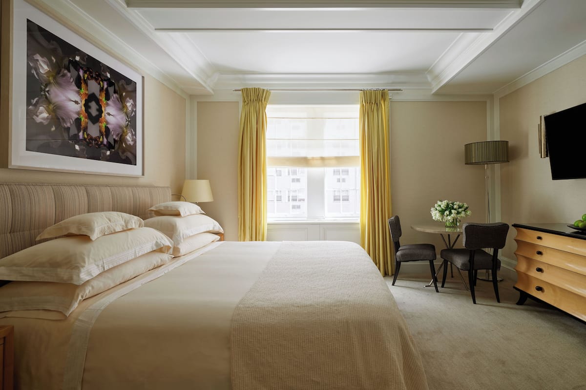 A hotel room with a large bed, a desk with a chair, a TV, and a window with curtains.
