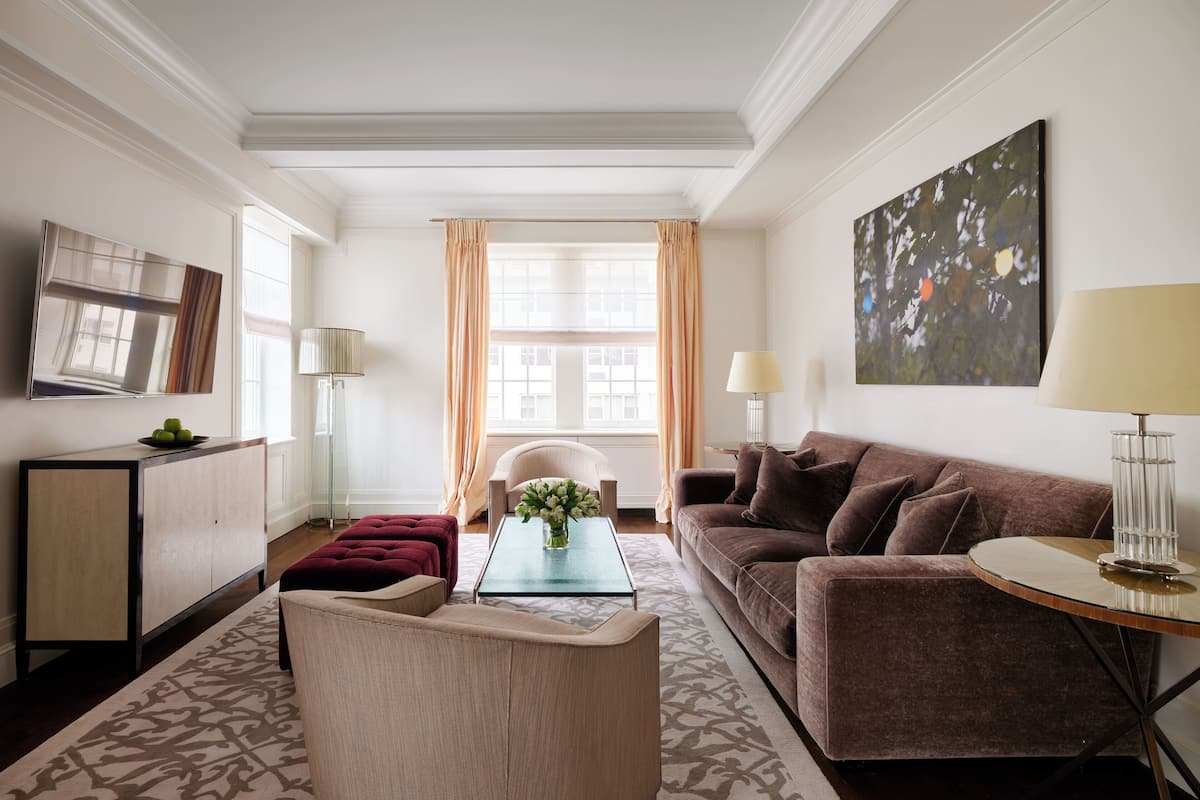 A modern living room with a sofa, armchair, and coffee table. There is a TV mounted on the wall, a lamp, and a painting.