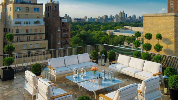 Una terraza en la azotea con mobiliario exterior, plantas en macetas y vistas a la ciudad.