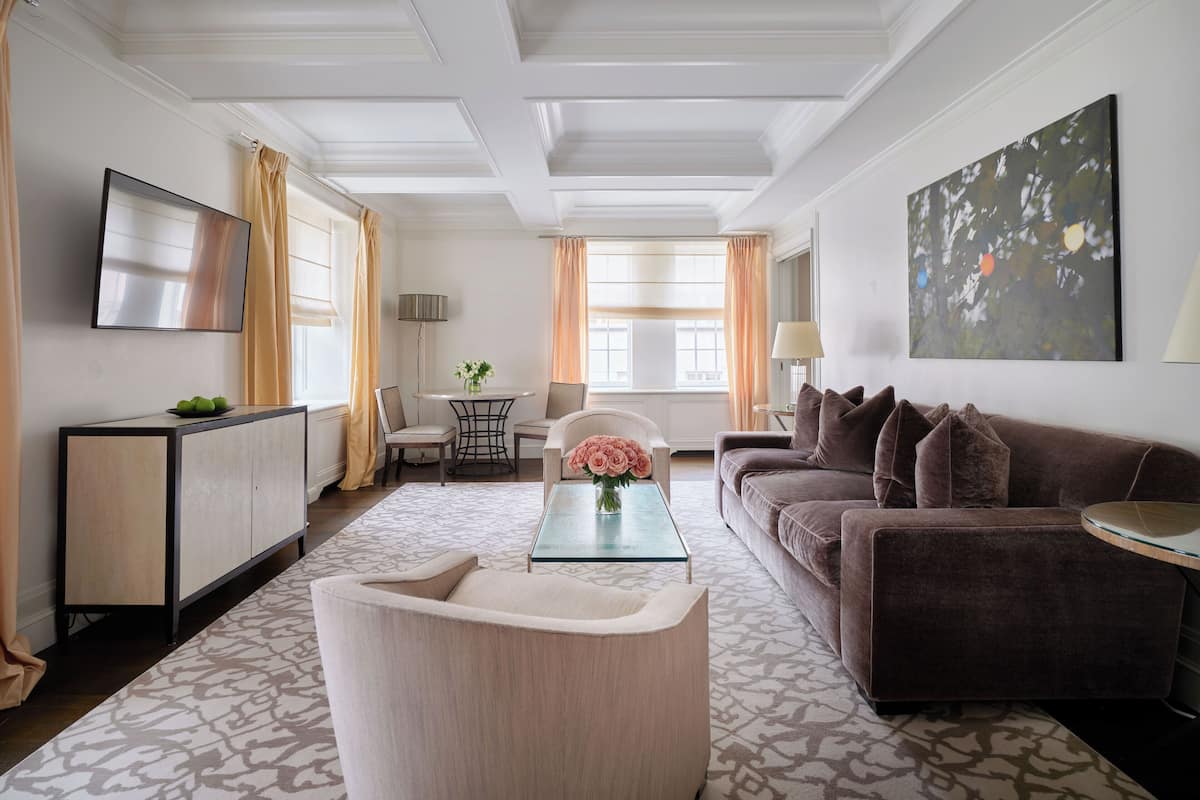 A modern living room with a sofa, armchair, and coffee table. There is a TV mounted on the wall, a lamp, and a painting.