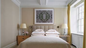 A neatly arranged bedroom with a large bed, two bedside tables with lamps, a framed artwork above the bed, and a window with curtains.