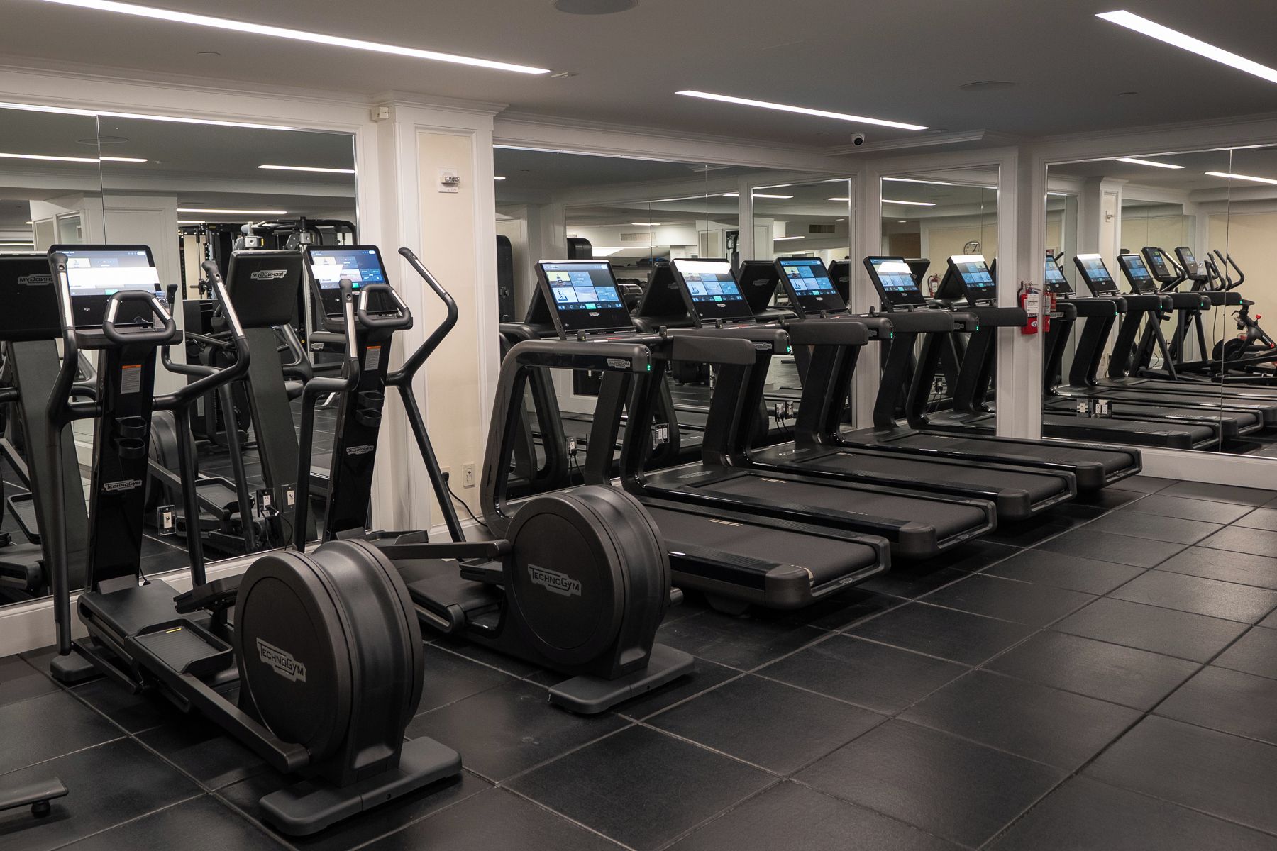A gym with multiple treadmills and elliptical machines, each with a digital display.