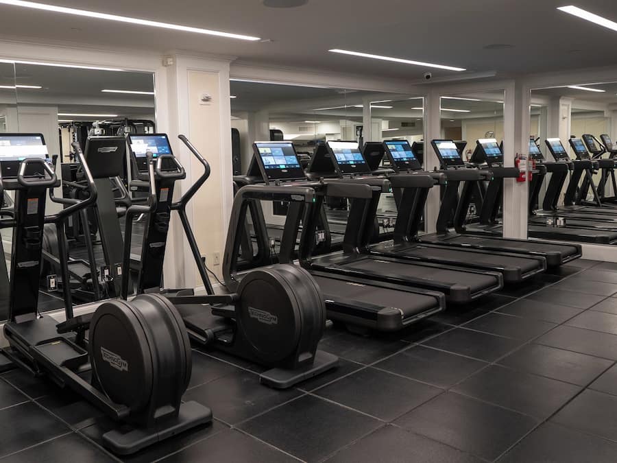 A gym with multiple treadmills and elliptical machines, each with a digital display.