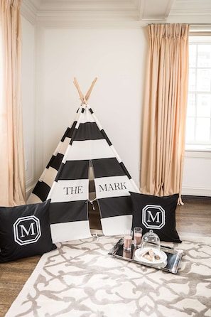 Een knus ingerichte kamer met een zwart-wit gestreepte tipi, een dienblad met snacks en drankjes, en bijpassende kussens met een monogram.