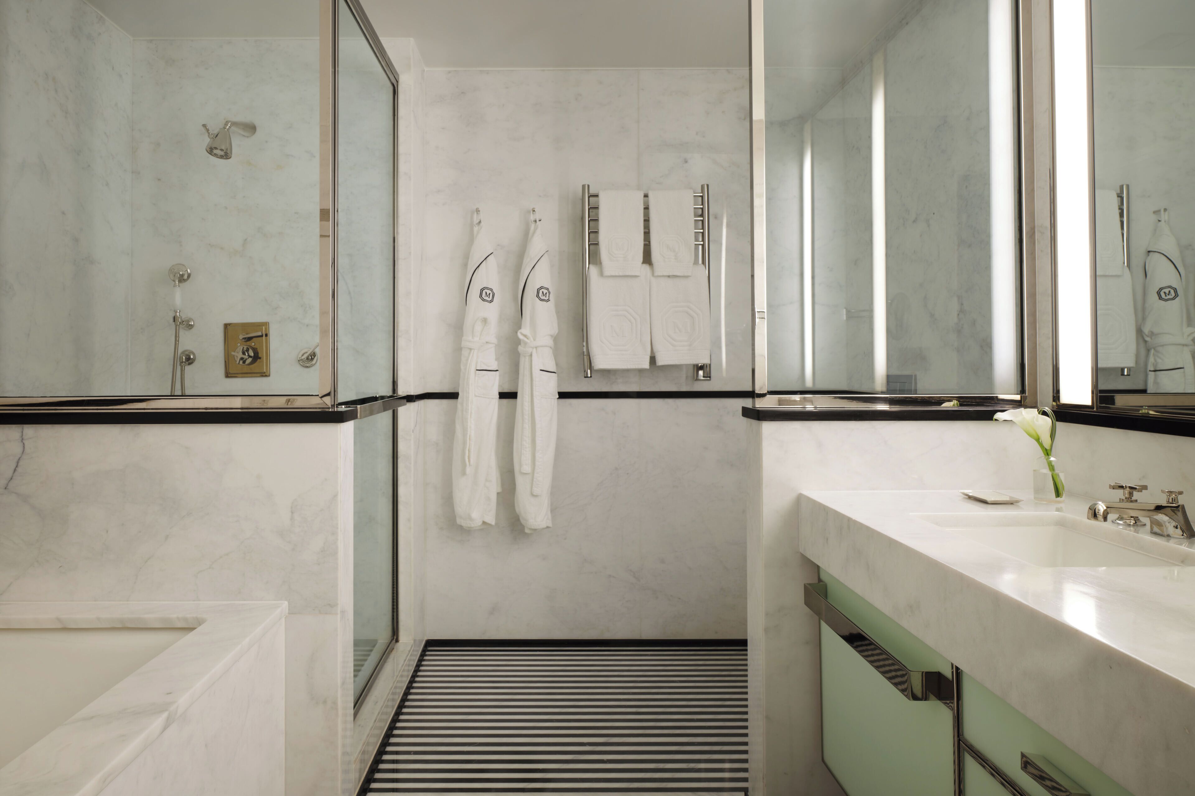 Un baño moderno con cabina de ducha de vidrio, un espejo grande y tocador con lavabo y toallero.