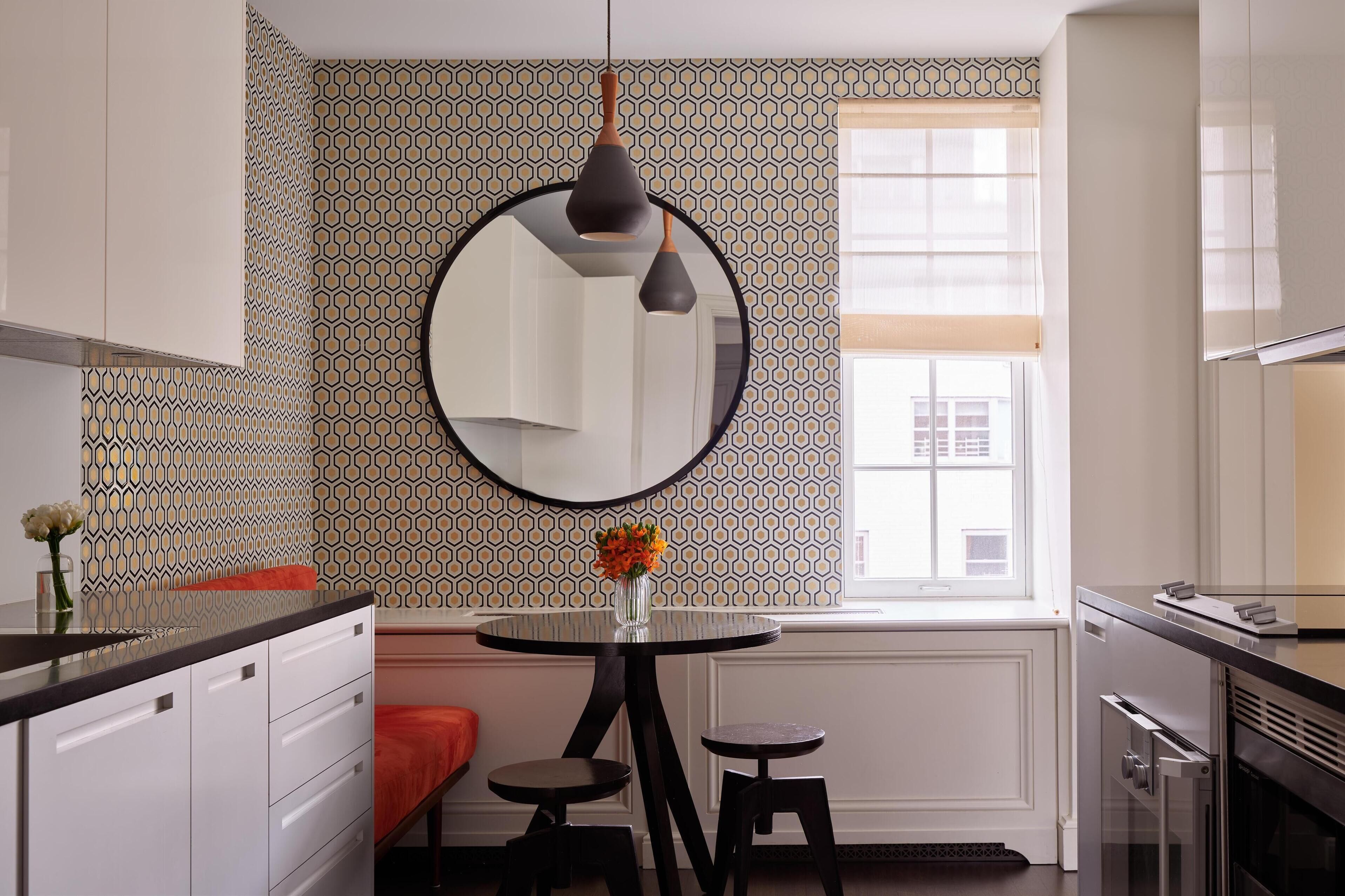 Une cuisine moderne avec une table ronde, deux tabourets, un luminaire suspendu et un grand miroir.