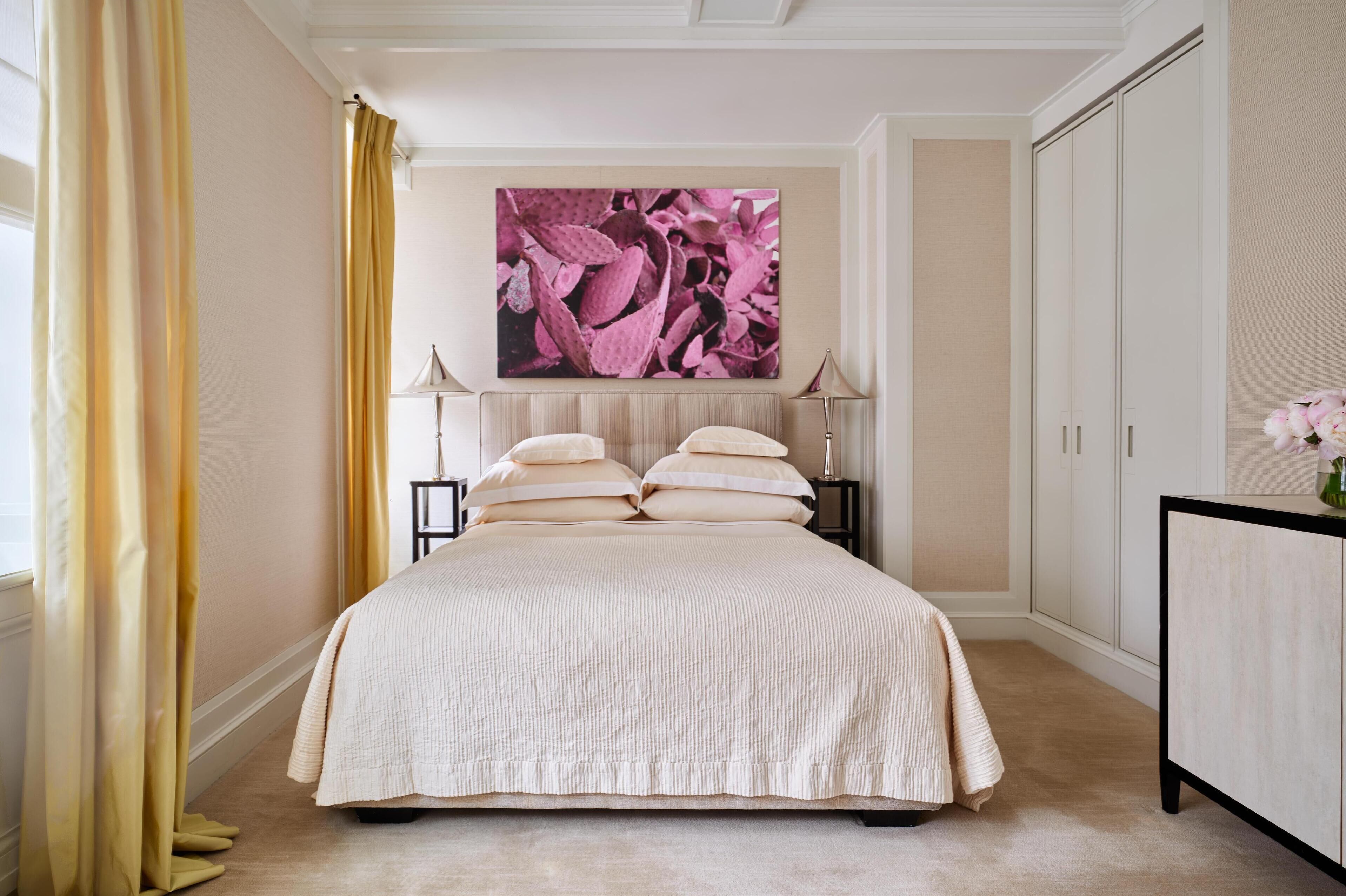 A bedroom with a large bed, two bedside tables, a nightstand, a dresser, and a large painting on the wall.