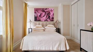 A bedroom with a large bed, two bedside tables, a nightstand, a dresser, and a large painting on the wall.