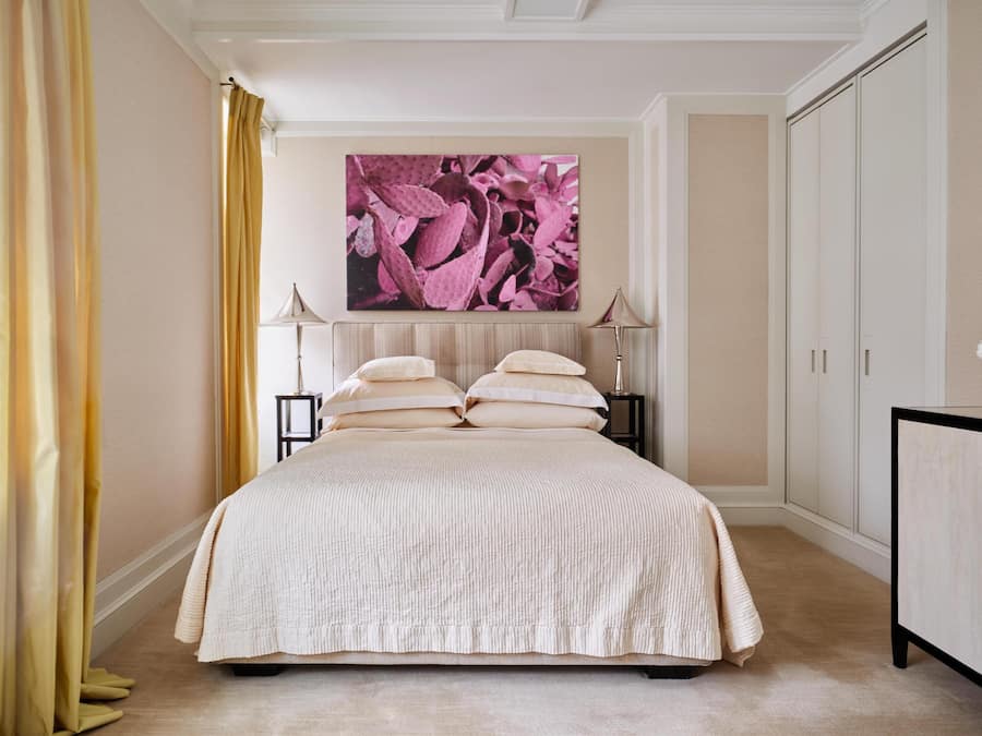 A bedroom with a large bed, two bedside tables, a nightstand, a dresser, and a large painting on the wall.